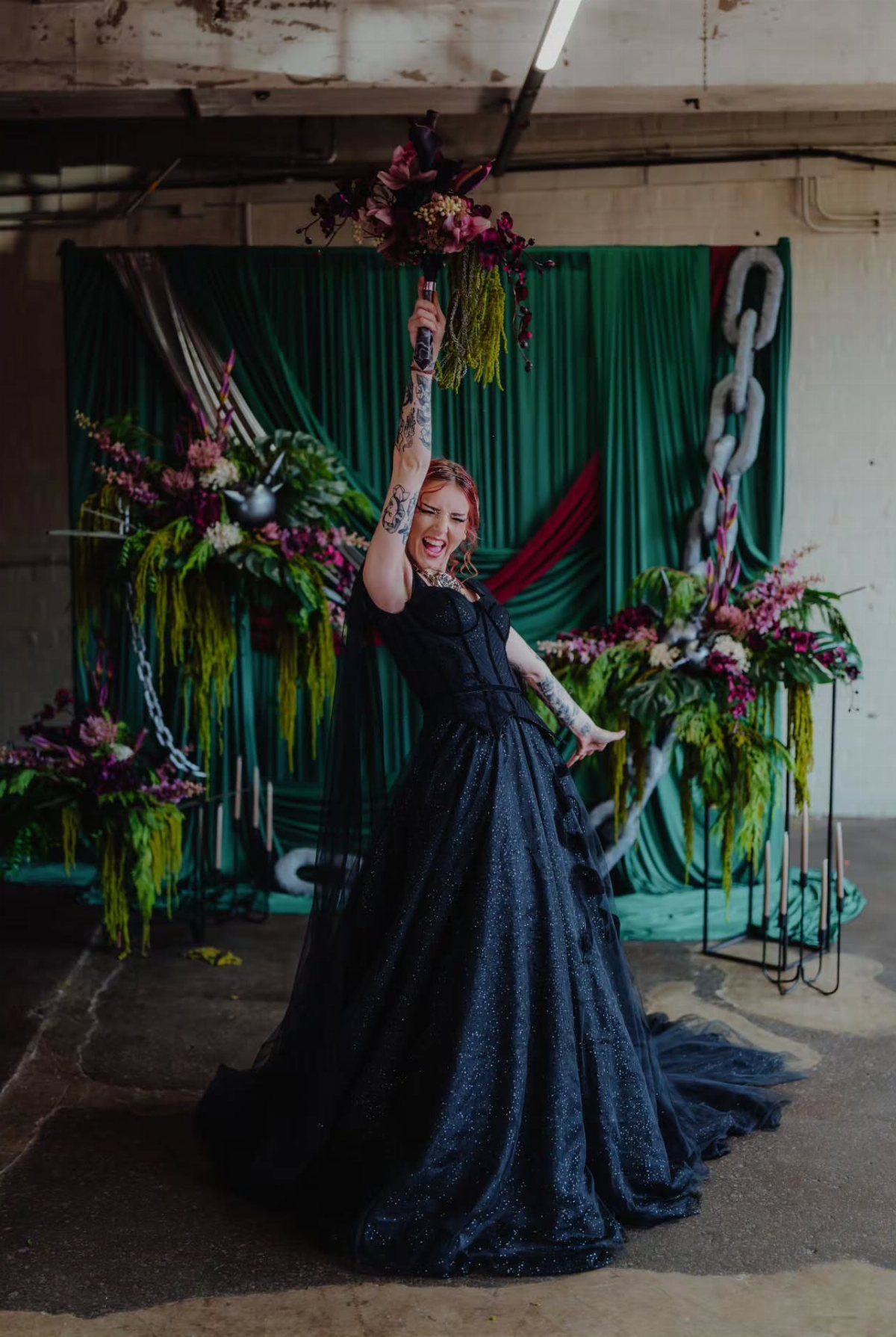 A woman in a sparkling black ballgown wedding dress poses with a bouquet against a green backdrop.