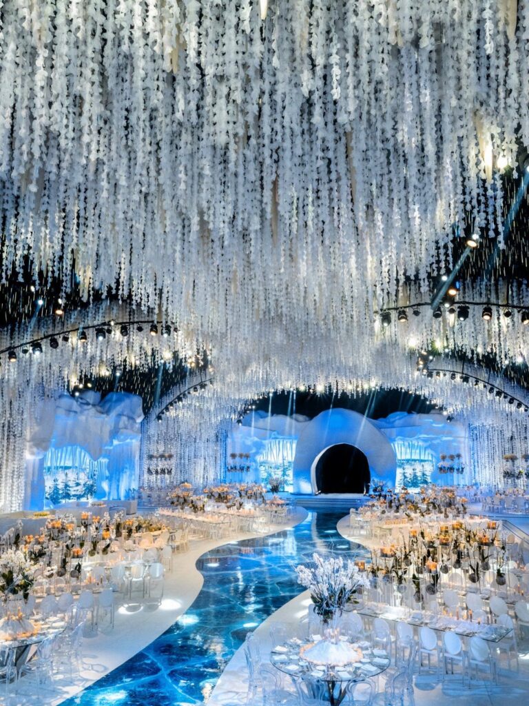 Elaborate winter wonderland wedding reception with white hanging decorations and a glowing blue aisle.