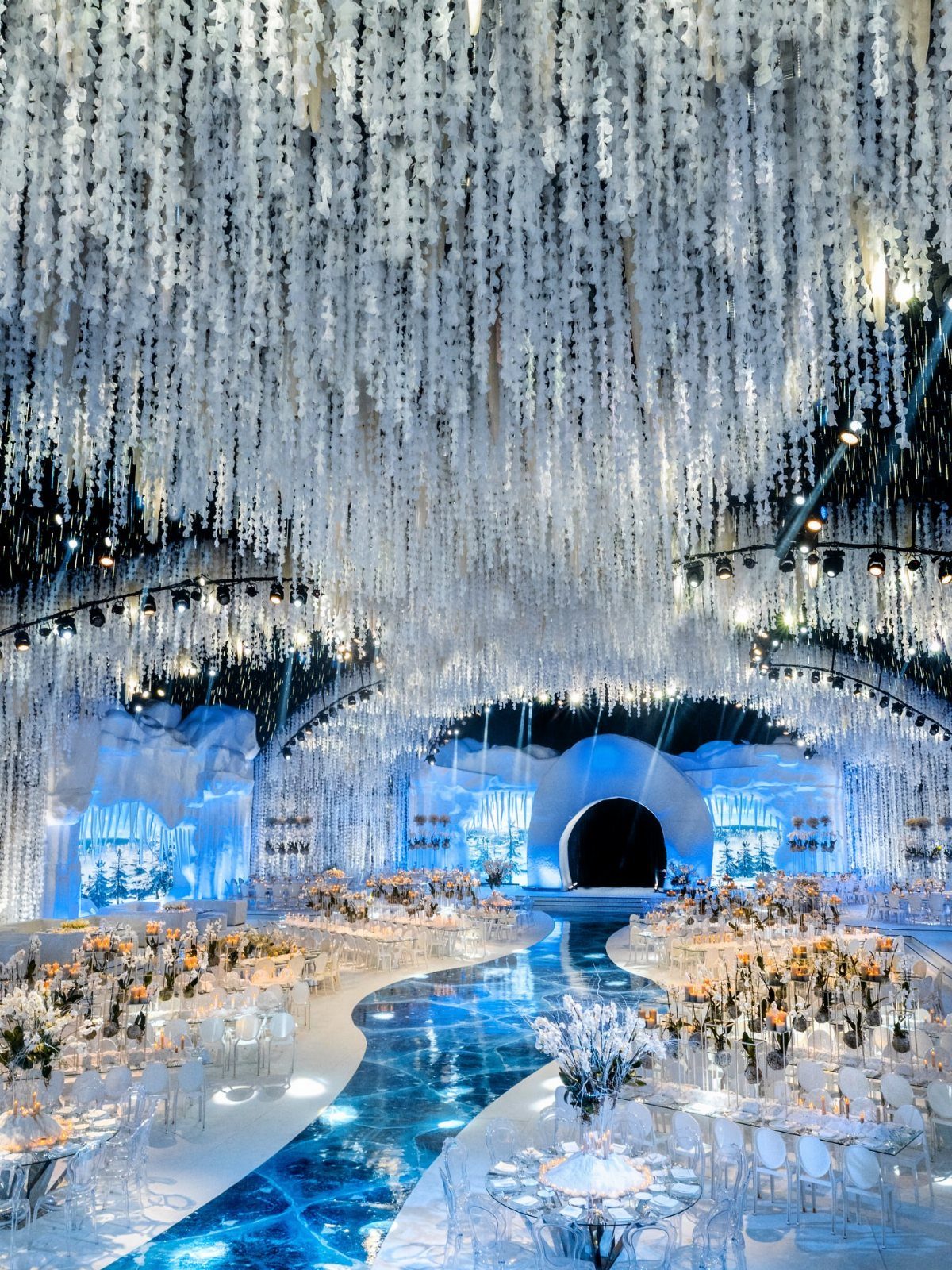 Elaborate winter wonderland wedding reception with white hanging decorations and a glowing blue aisle.