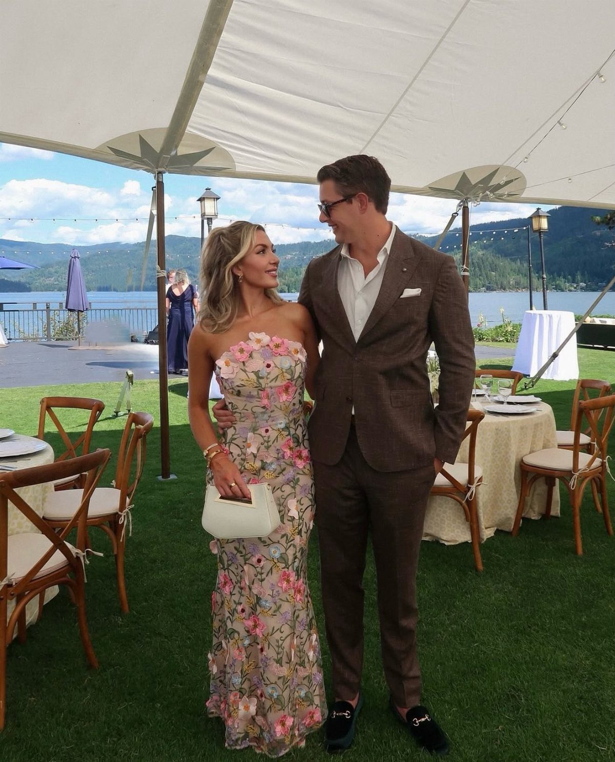 A man in a brown suit and a woman in a floral dress posing outdoors.