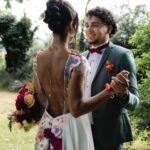 A bride in a floral embroidered dress and a groom dancing in a green garden.