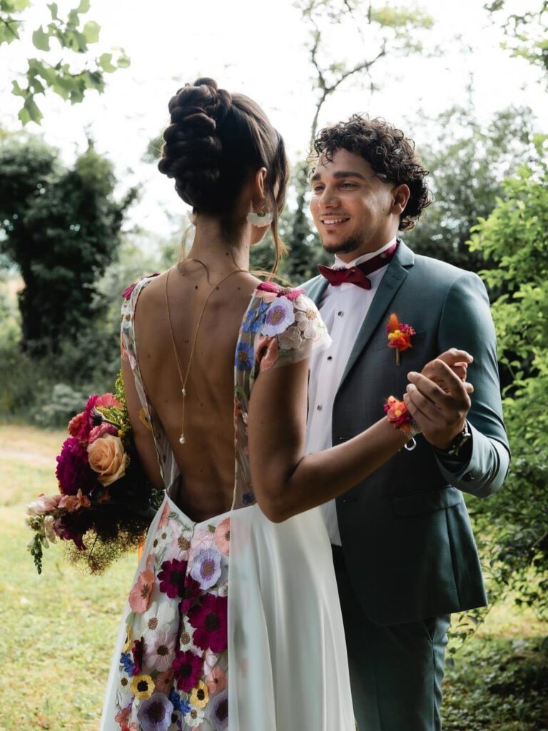 A bride in a floral embroidered dress and a groom dancing in a green garden.