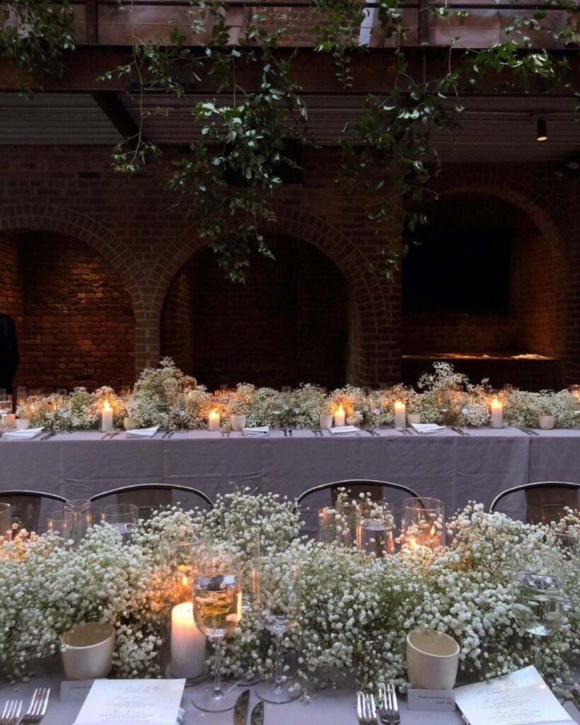 White baby's breath flowers and small candles arranged as a long garland on a dining table.
