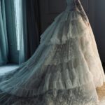 A white lace ball gown with tiered ruffles and a long train in a room.