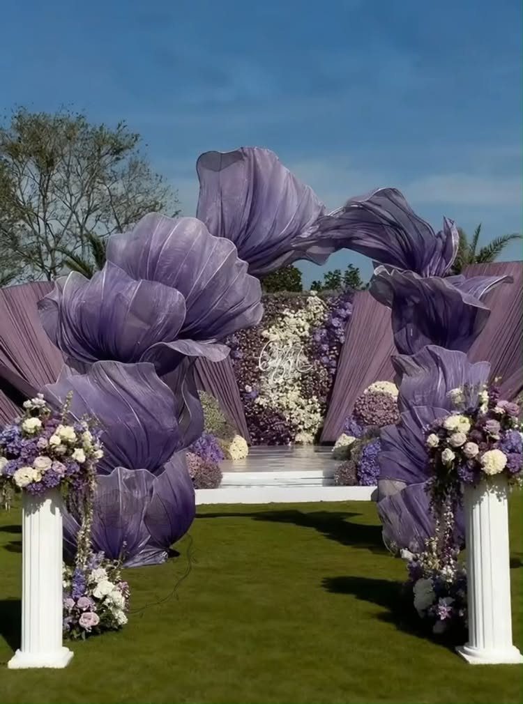 Large purple fabric archway and floral arrangements decorating an outdoor wedding ceremony setup on a lawn.