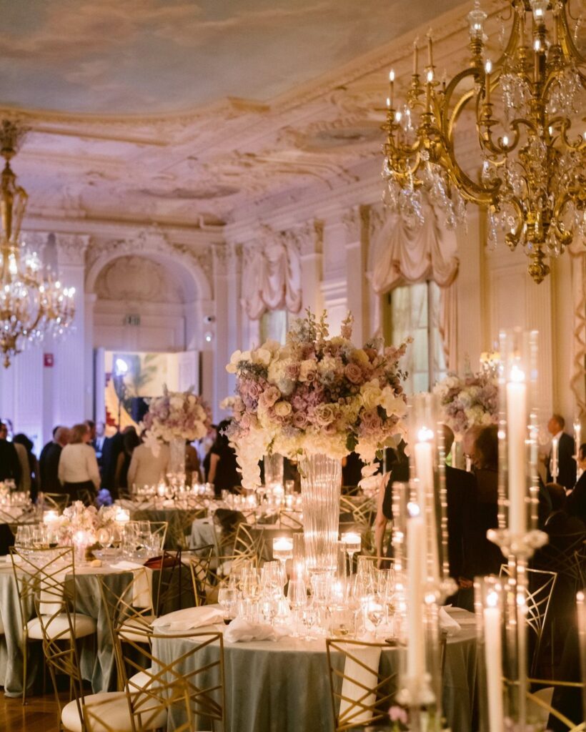 Elegant ballroom decorated for a wedding with candlelit tables and large floral centerpieces.