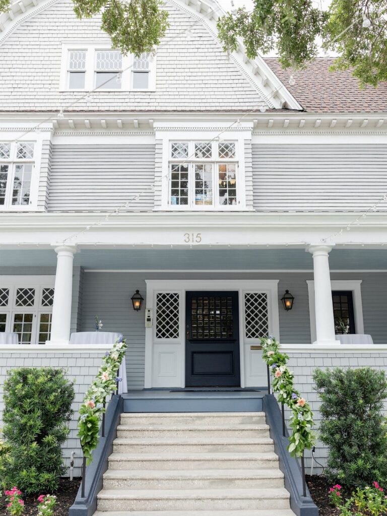 A light grey house with white columns and a front porch decorated with floral garlands.