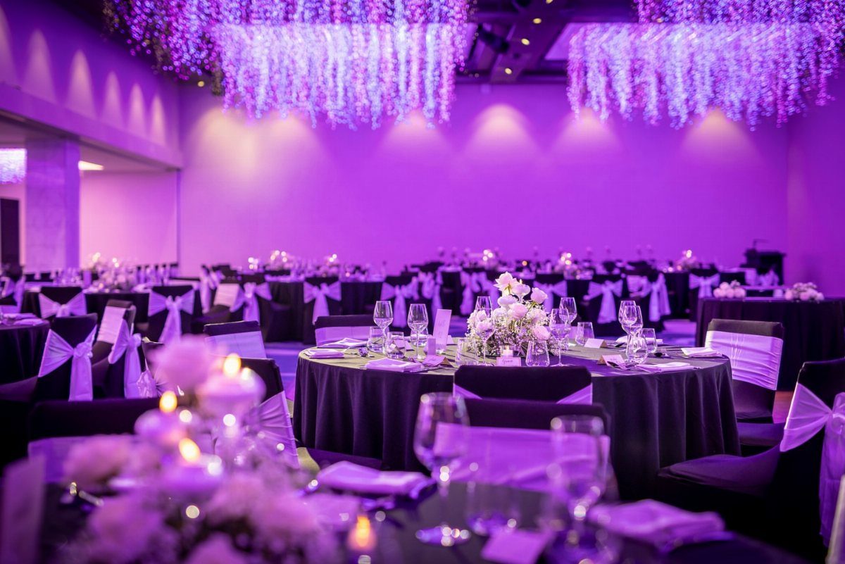 Banquet hall decorated with purple uplighting, black linens, and hanging floral arrangements for a wedding.