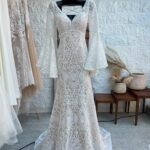 A white lace wedding dress with long bell sleeves hanging on a black hanger.
