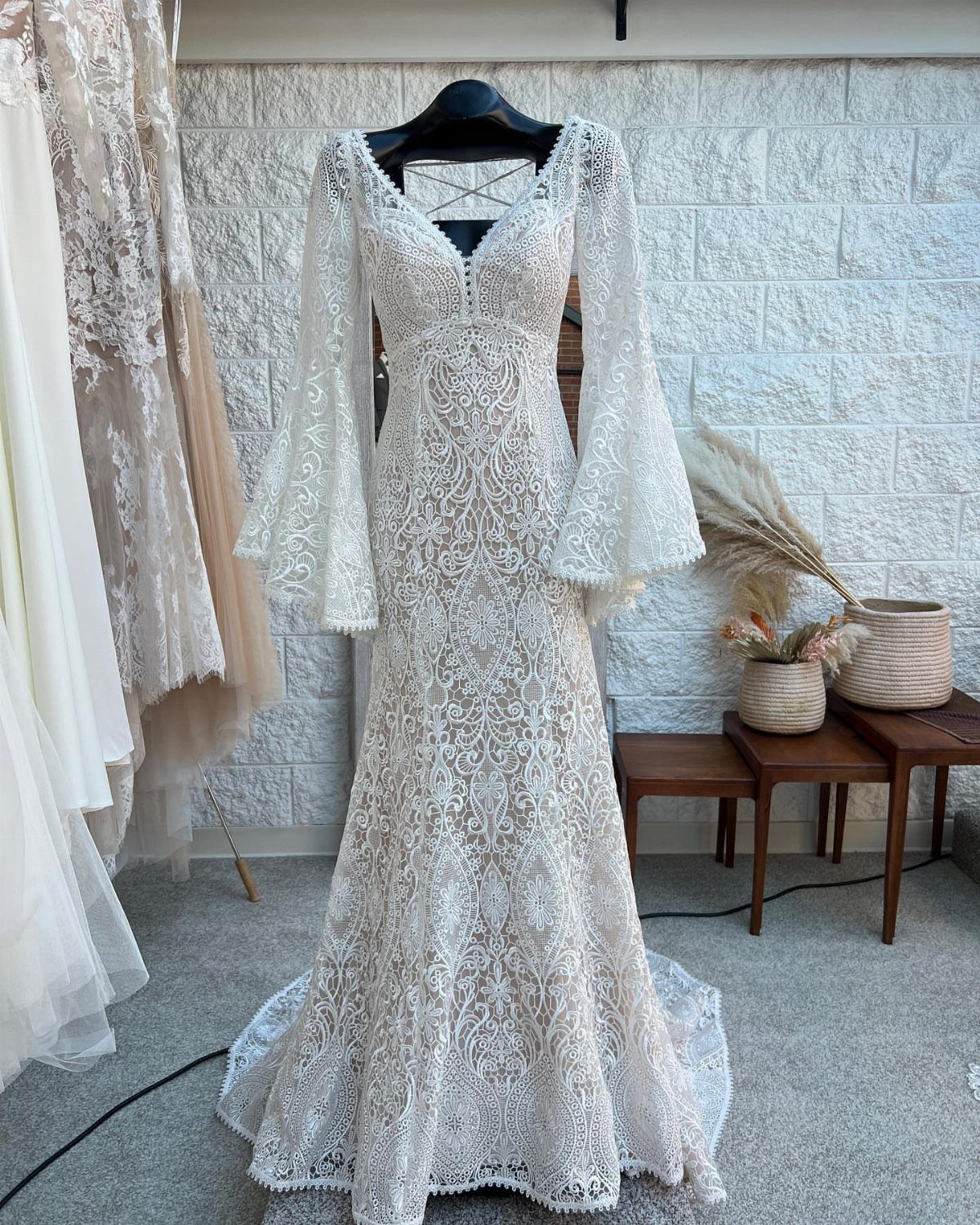 A white lace wedding dress with long bell sleeves hanging on a black hanger.