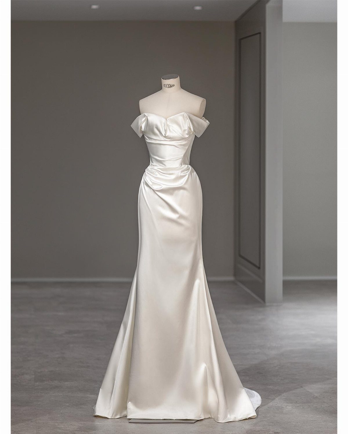 A white satin wedding dress with off-the-shoulder sleeves displayed on a mannequin.